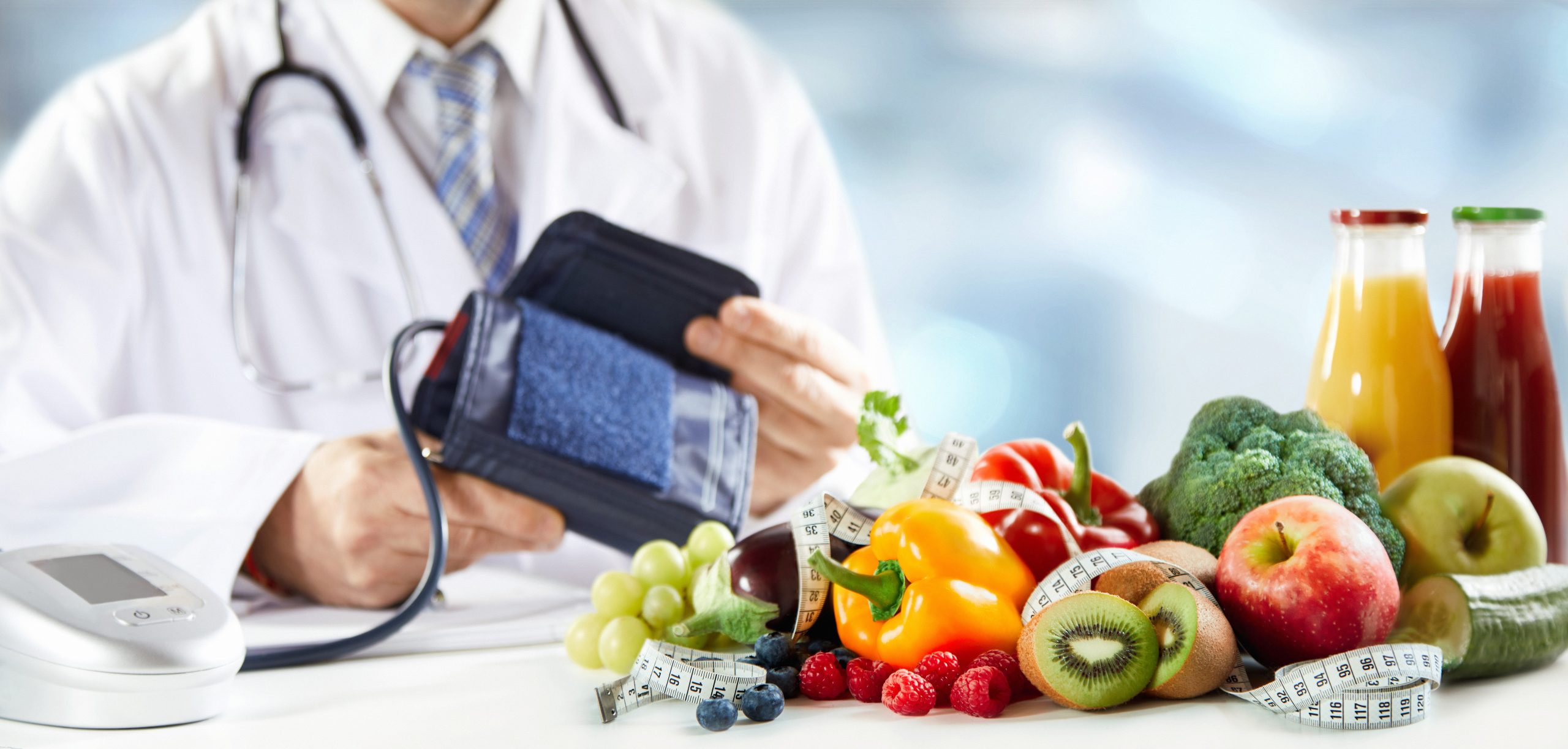 Healthy diet and blood pressure concept with an assortment of colorful fresh fruit, vegetables and smoothies in front of the hands of a doctor holding a sphygmomanometer or cuff in a panorama banner